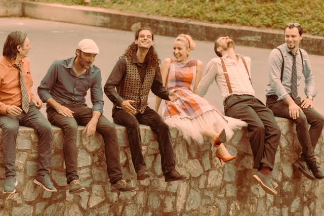 Bend sjedi na kamenom zidiću i smije se